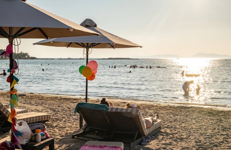people lying on beach chairs on a sandy beach in front of the sea at Balux, Glyfada