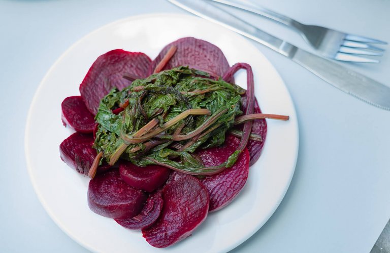Sliced beetroots with their leaves on a white plate. 