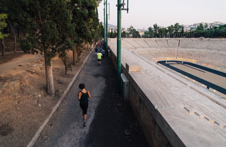 Woman running on a path next to an open marble stadium. 