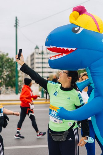 a female runner taking a selfie with Marthon's mascot, a blue dinosaur.