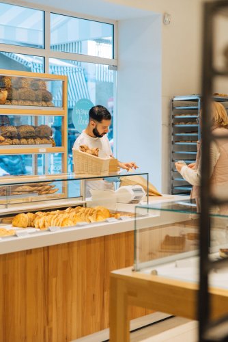 a woman buying bread from a man at a bakery shop, pastries on display.