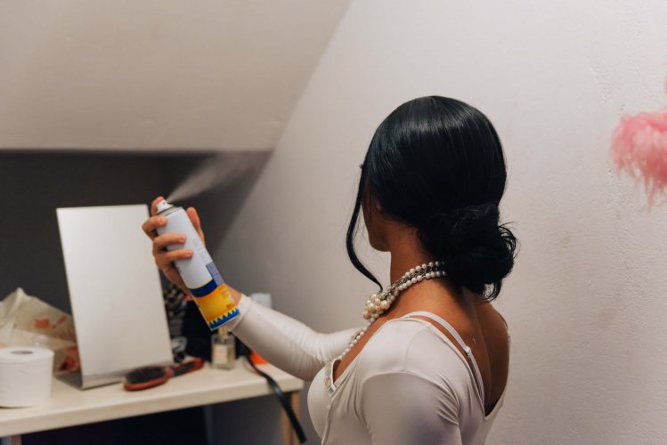 a drag performer in their dressing room spraying their hair.