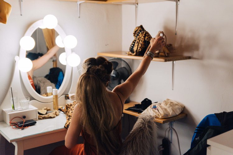 a drag performer in their dressing room, reaching for their high-heels.