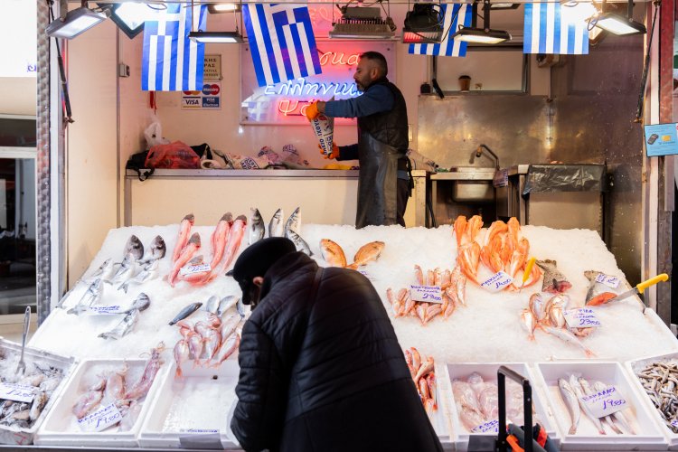 a stall with different fish and greek flags hanging.