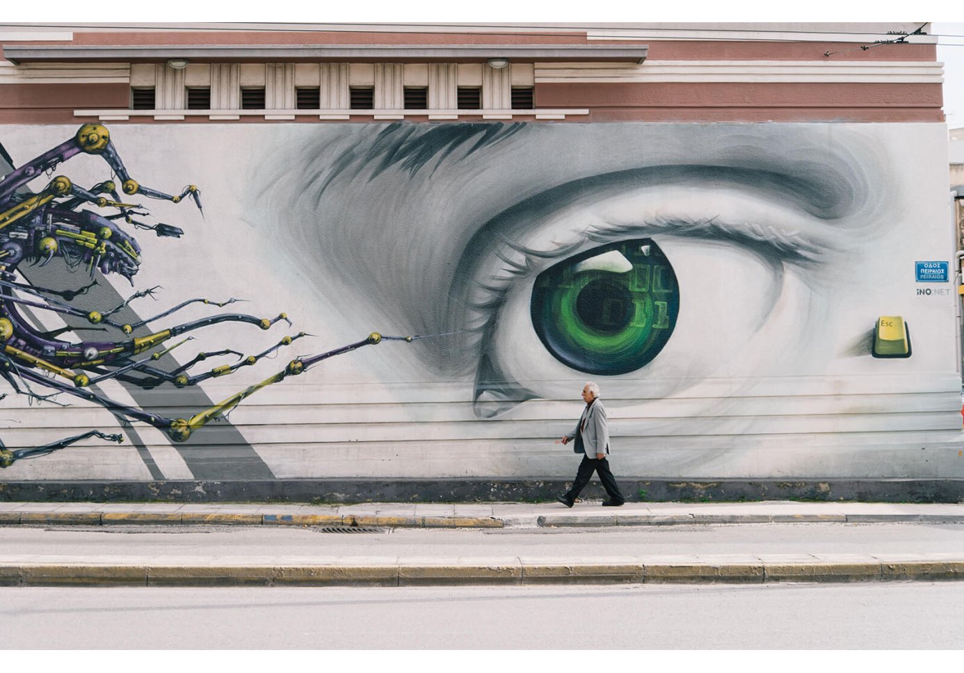 graffiti of a green eye on a wall and a person walking by.