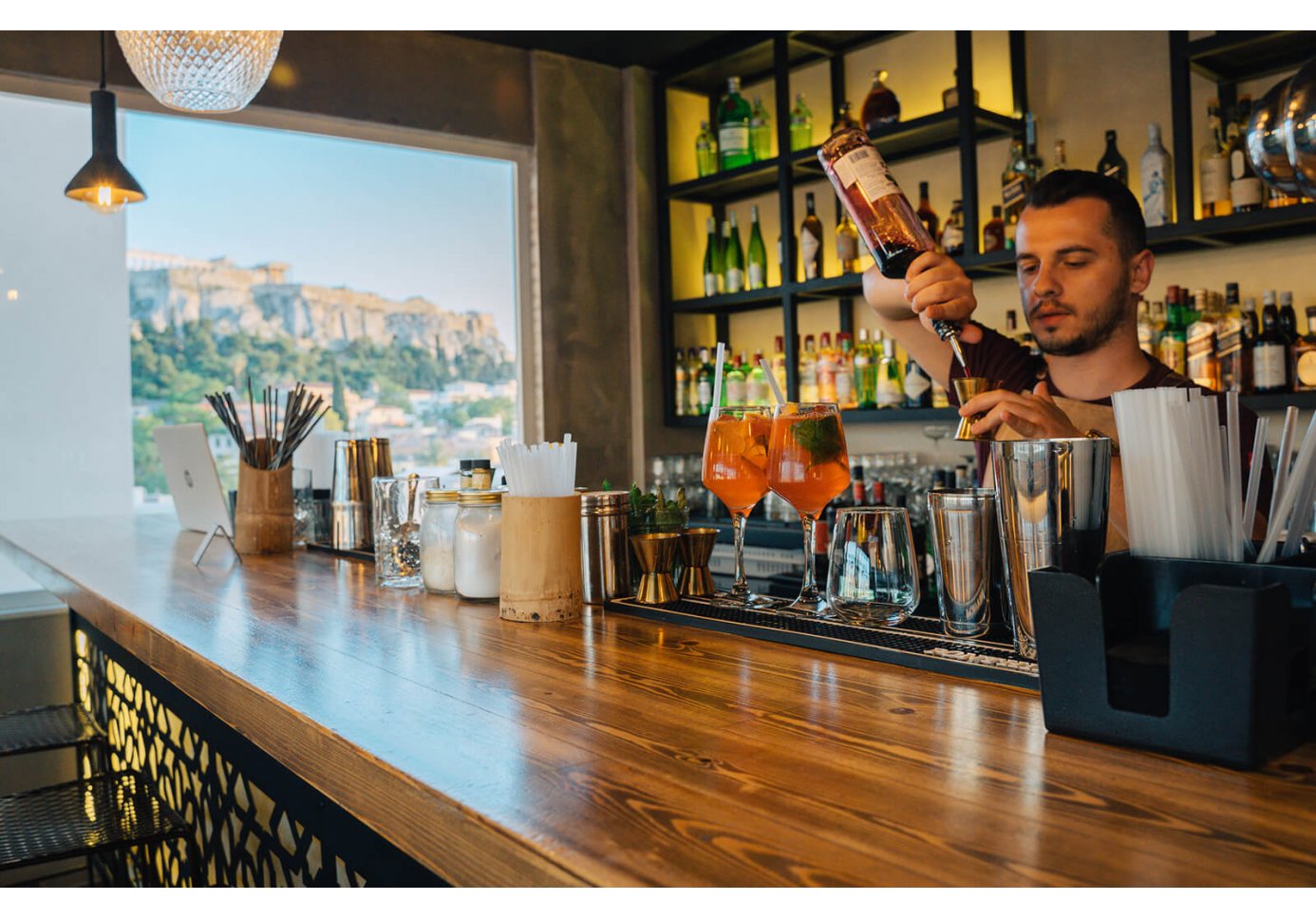 A barman behind the bar at Ciel in Athens making a drink with Acropolis in the background. 