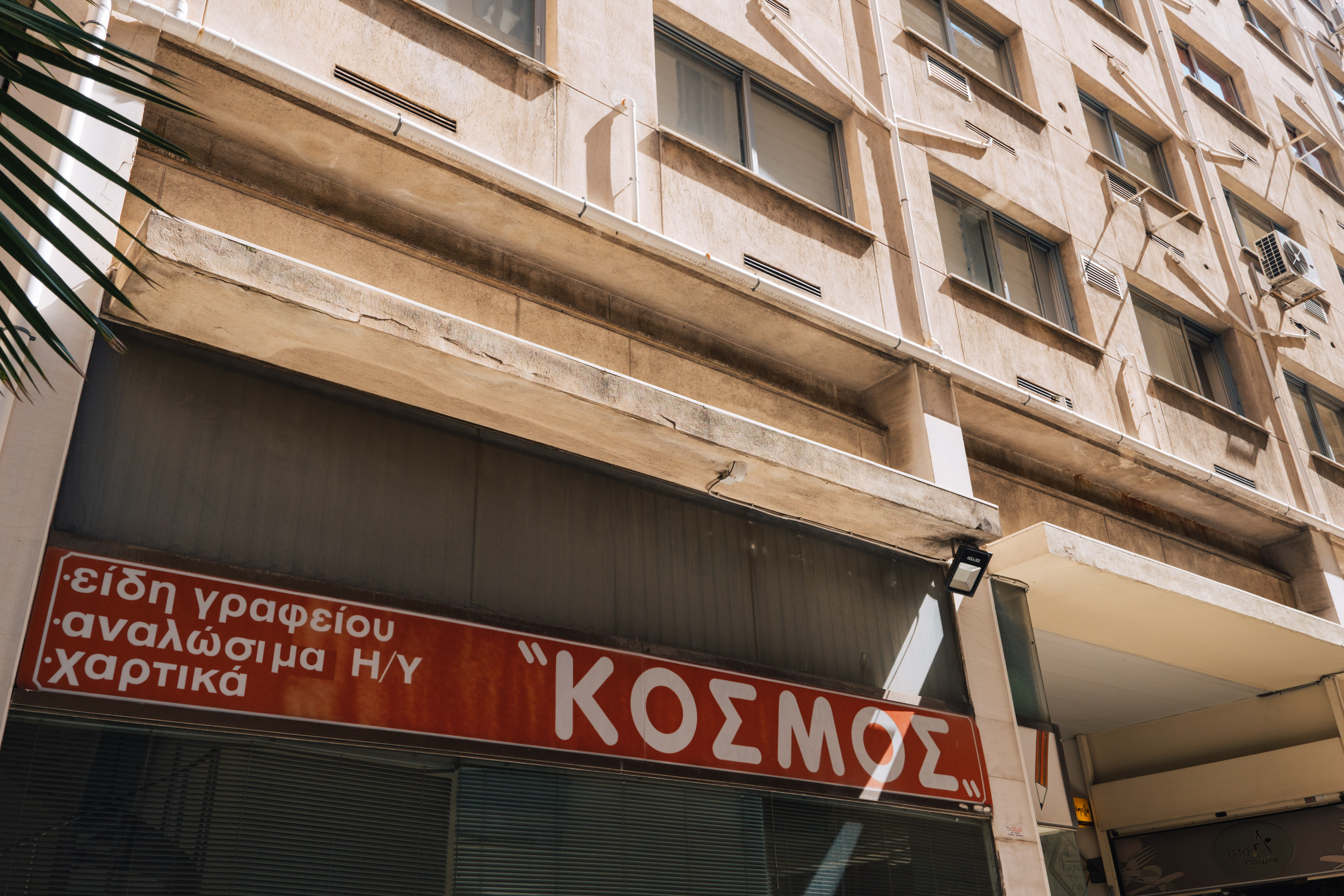 "ΚΟΣΜΟΣ" as in cosmos, world. San Serif madness in Pesmazoglou arcade. | Photo: Georgios Makkas 