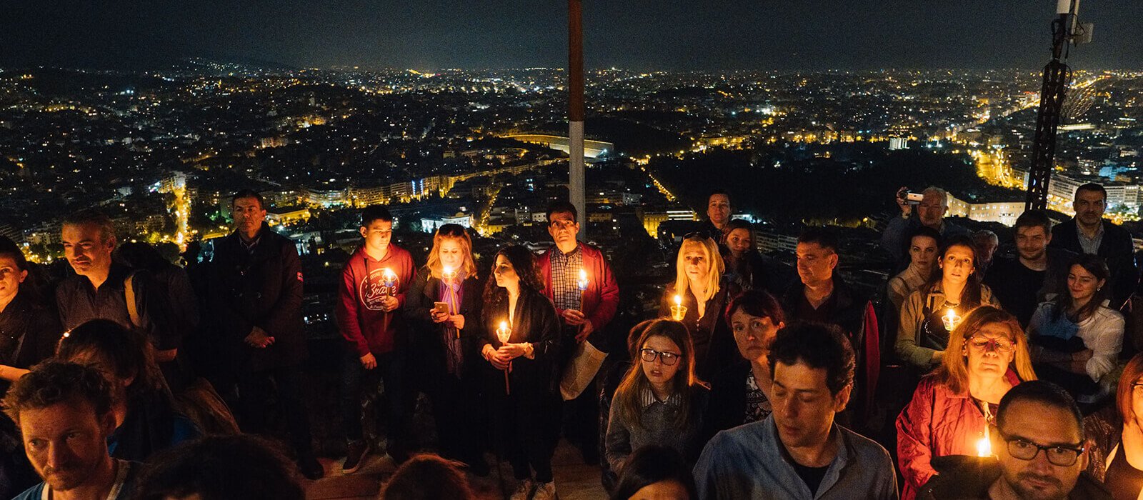 Group wearing bone conduction headphones during a midnight candlelit procession in Greece.