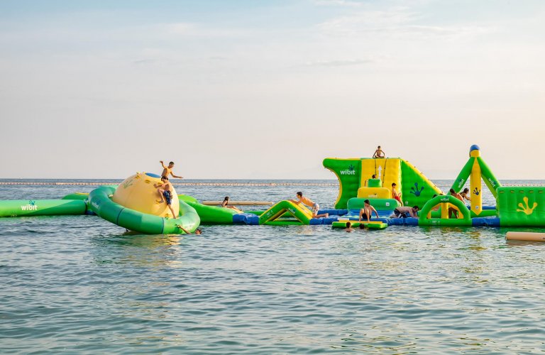Children playing in the sea on a green and yellow floating playground