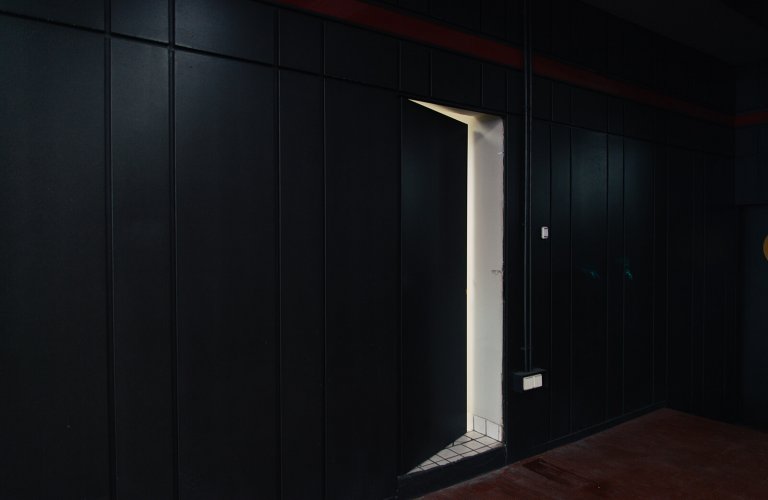 a black hidden door on a black door opened revealing a white space