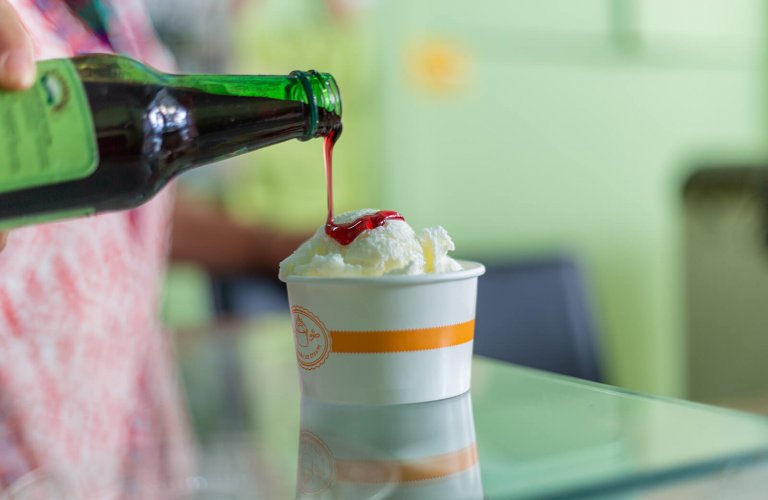 syrup being poured on a cup of ice cream from a bottle