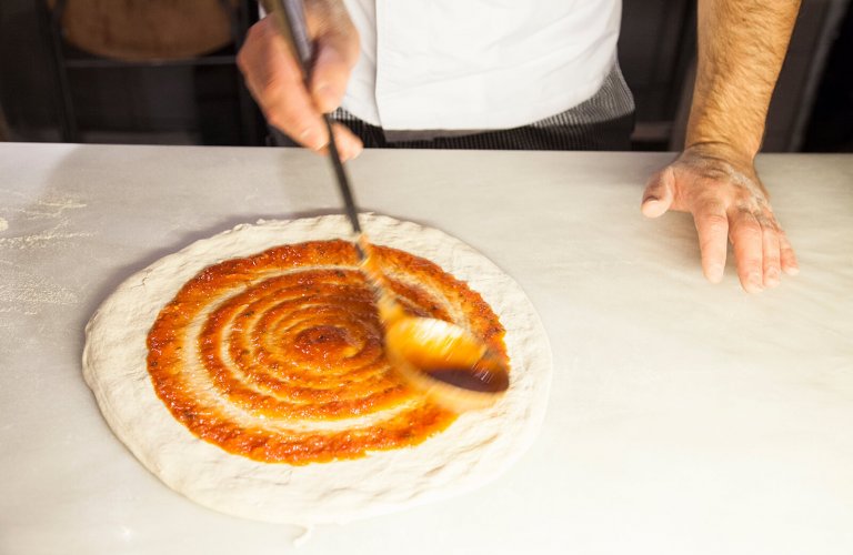 A man spreading sauce on dough with ladel at Capanna restaurant in Athens. 