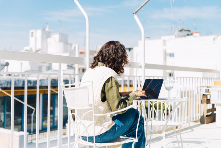 A woman working on her laptop at a table on her balcony