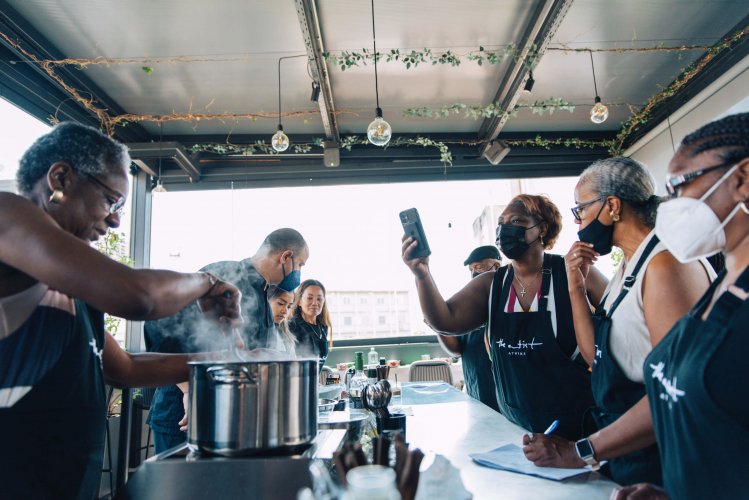 a group of people attending a cooking class over a kitchen counter, a woman taking a photo