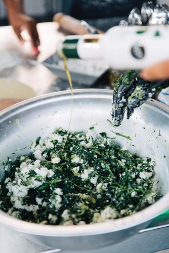 a chef adding olive oil to a mixture of green herbs and feta cheese for spanakopita