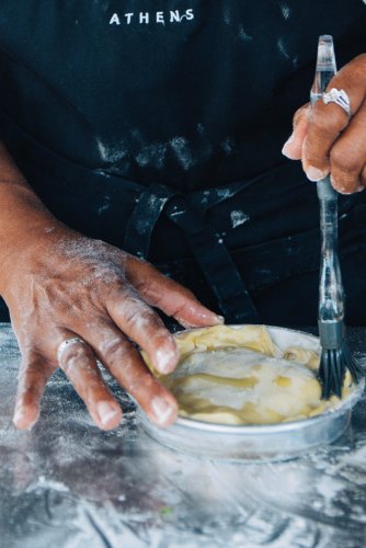 woman's hands spreading olive oil on a pita with a kitchen brush, flour all over