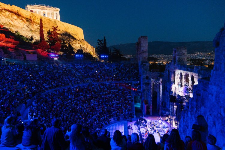a crowd at the Odeon of Herodes Atticus in Athens, blue lighting, the Parthenon at the background