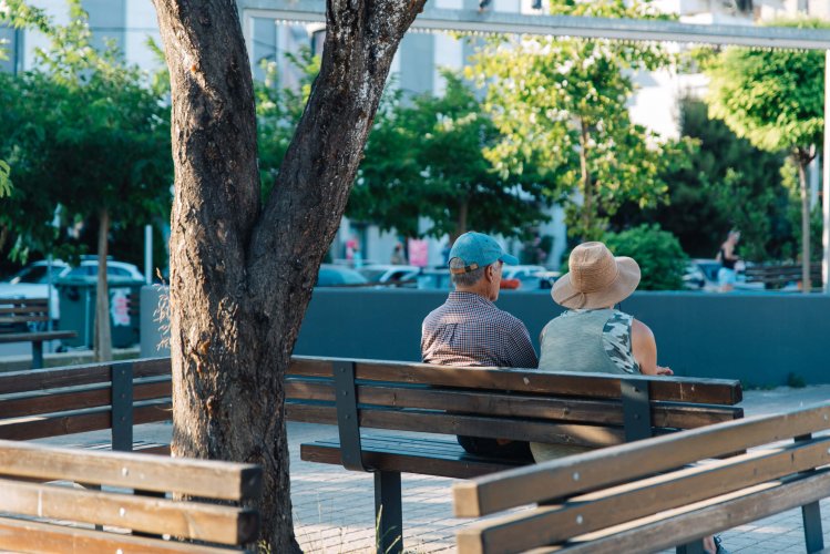 two old people sitting on a bench before a tree.