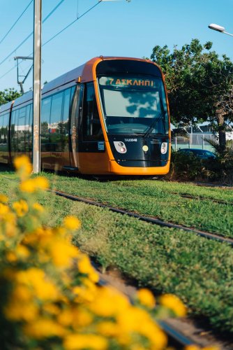 an orange tram on the move, flowers and trees around.