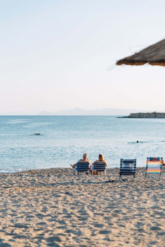 two people sitting on beach chairs, two empty chairs, the sea.