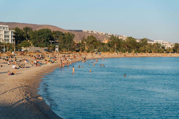 a crowded beach, people swimming, sunbathing, a mountain at the background.