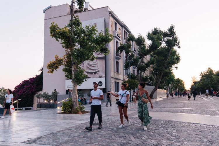 three people walking down Areopagitou street passing by the Acropolis' Museum.