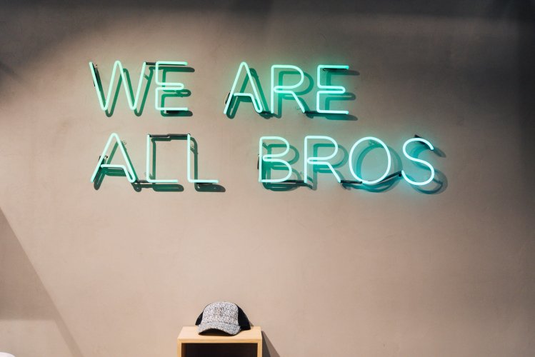 a neon blue sign writing "we are all bros".