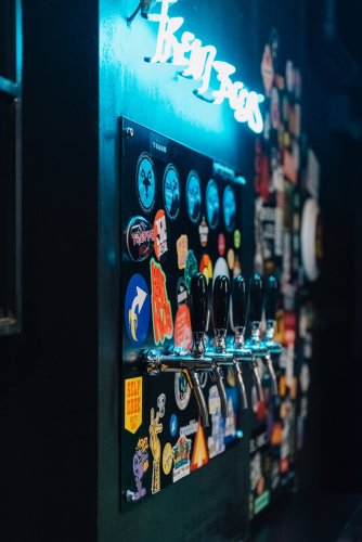 several beer pumps and stickers, a white neon sign on a blue wall.