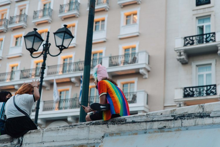 A marcher wearing a rainbow flag T-shirt sitting on Syntagma's steps.