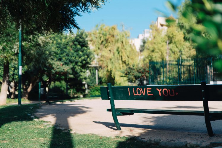a green bench in a park with a red lettered "I love you" written on it.