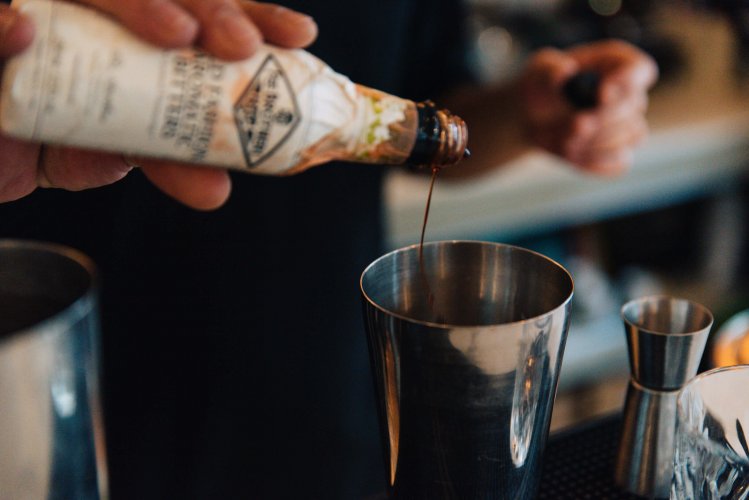 a barman pouring hot sause in a cocktail mixer. 