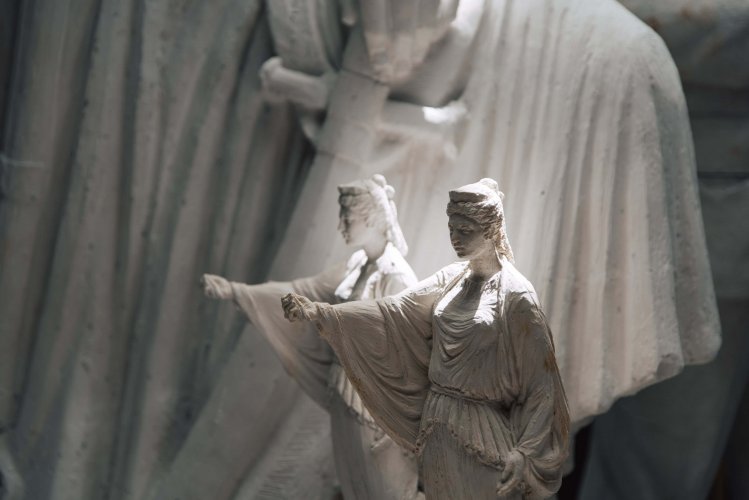 two small scaled female figured statues, detail of a sword on the background.