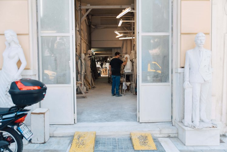 entrance to a sculpture studio, the artist inside, two statues and a motorbike on the outside.