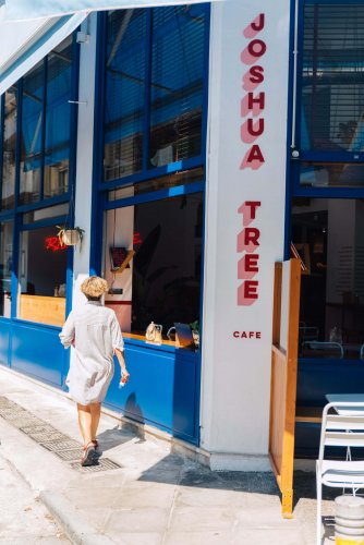 the blue and white entrance of a brunch place, red letters that read "joshua tree cafe", a woman passing by