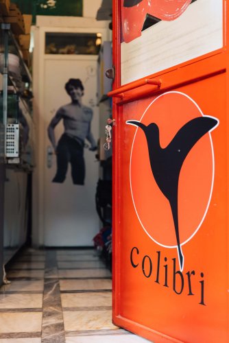 an orange open door with the drawning of a hummingbird, letters reading "colibri", an other door at the background with the poster of man
