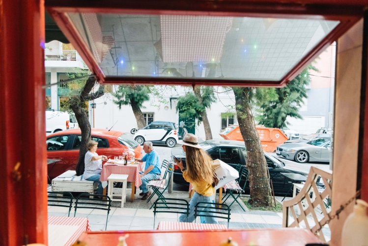 an older couple enjoying their meal at a table outside of the restaurant, a woman passing by