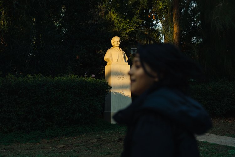 a photo focused on a statue lit by afternoon's light, a girl passing in front of it