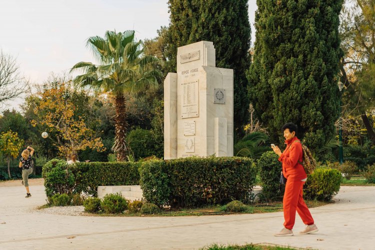 a woman in red walking in a park, kids playing with a ball at the background.