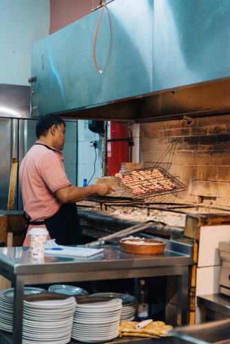view of a grill house's kitchen, a man turning chops on the grill. 