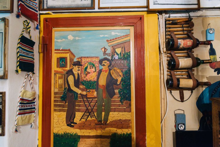 a vintage painting on a door, bottles of wine on the wall next to it. 