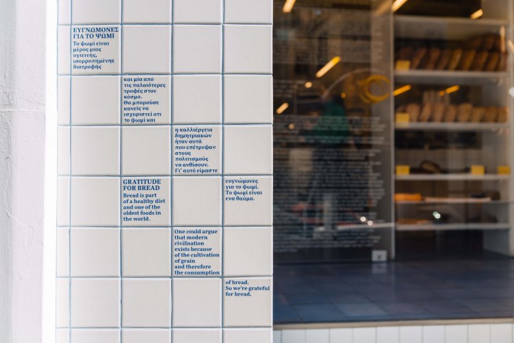 a white wall with blue lettering and loafs of bread on display at the background.