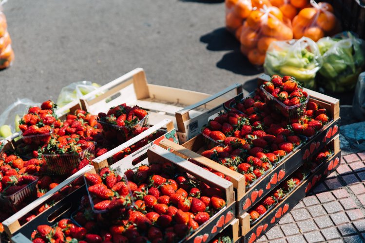 Baslets with strawberries and bags with oranges and zucchini on the pavement.