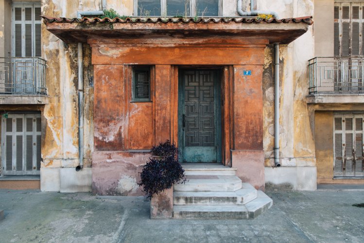 an old orange entrance with blue door and window, plants in front of it.