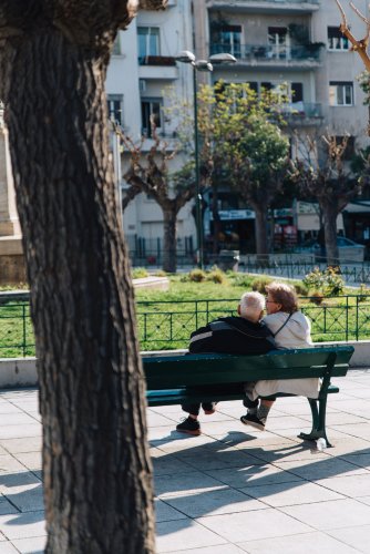 an elderly couple sitting on a bench at a square.