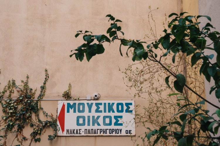 a sign on a wall that reads "musical instruments store Nakas-Papagrigoriou", trees around.
