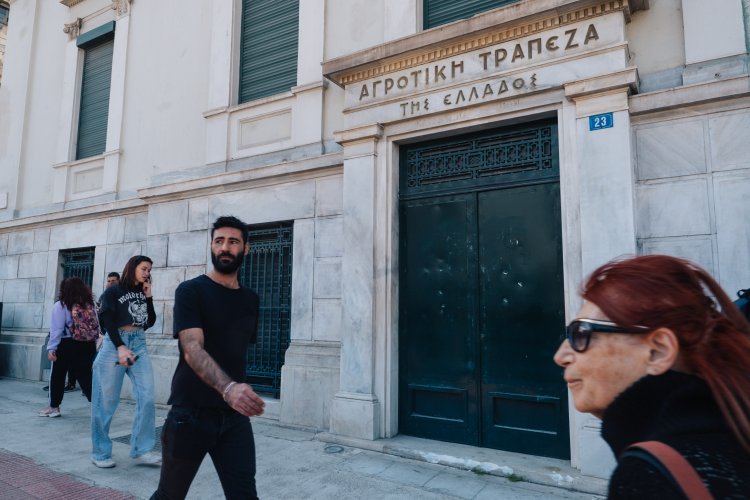 people passing by an old building with a sign that reads "Agricultural Bank of Greece"