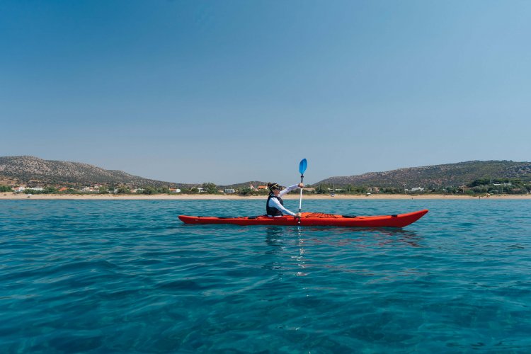 a woman kayaking, the beach behind her.