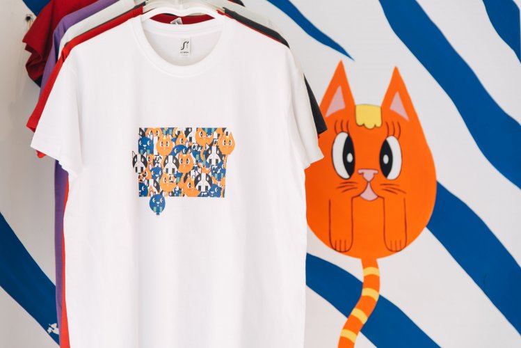 colored t-shirts on a rack in front of a blue/white wall with a drawing of an orange cat
