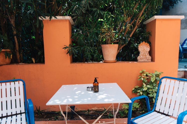 a pair of chairs and a table in front of an orange wall and trees.