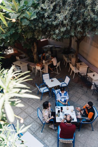 a bar's garden, people sitting in the tables, trees above them.